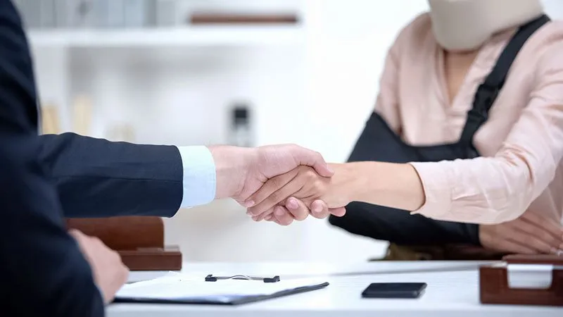 An accident attorney shaking hands with an injured client during a legal consultation.
