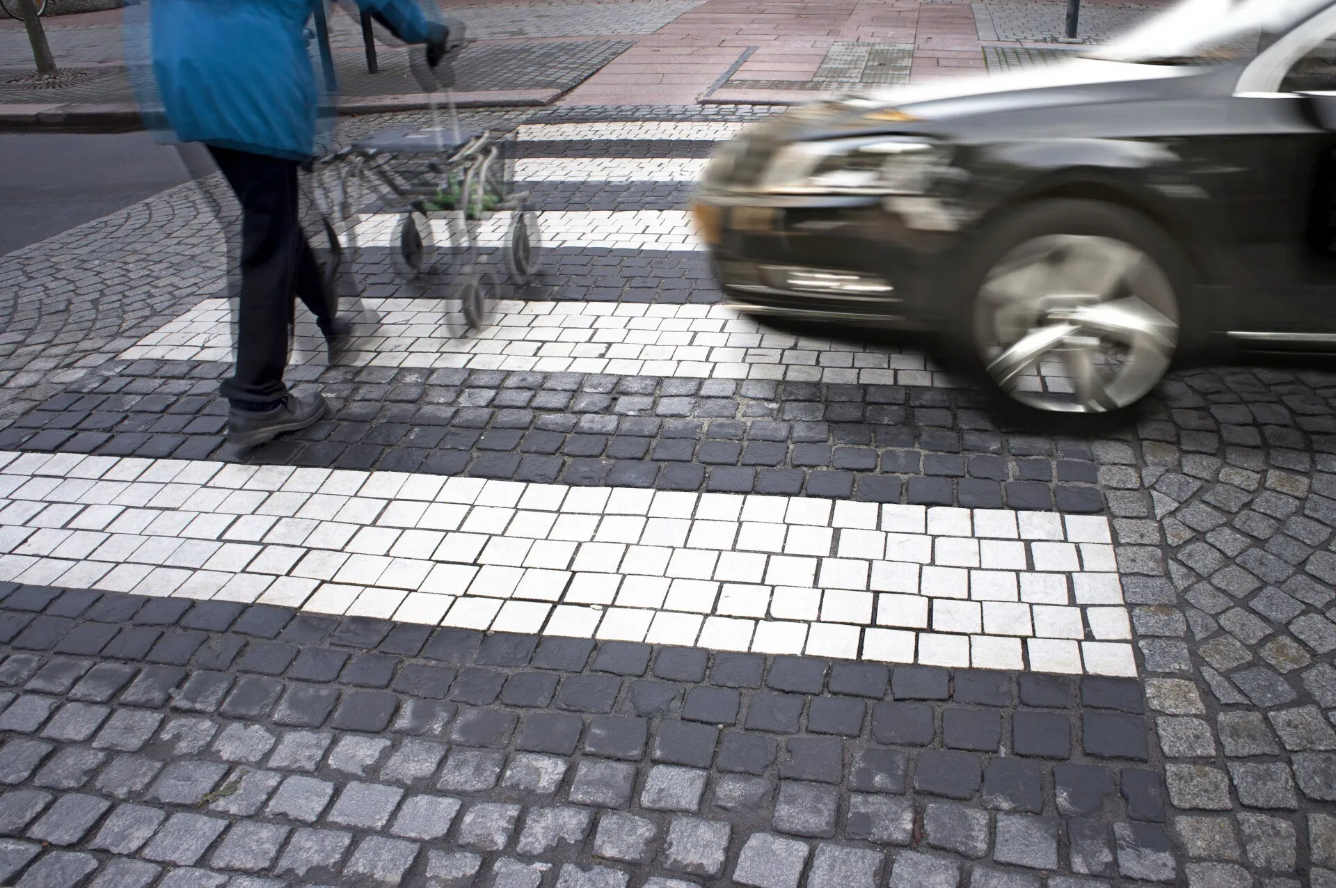 A car speeding near a pedestrian crossing with a person walking.