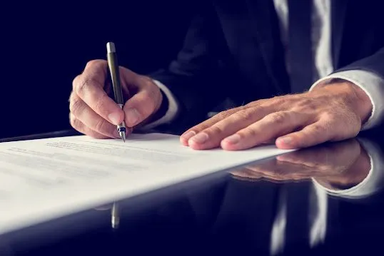 Professional signing a legal document with a pen at a desk
