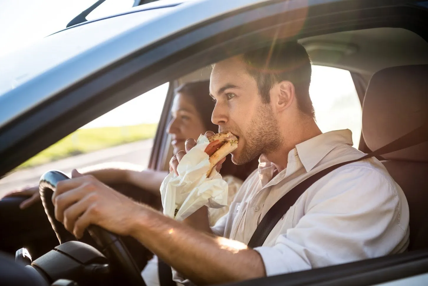 A man eating a sandwich while driving a car.