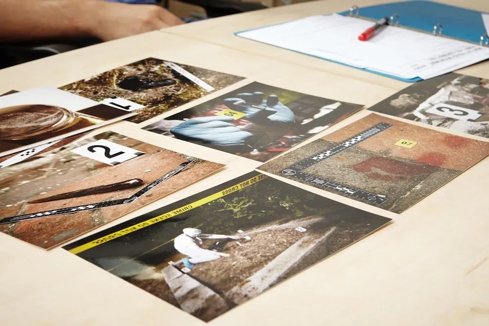 Crime scene photographs laid out on a table with a binder.
