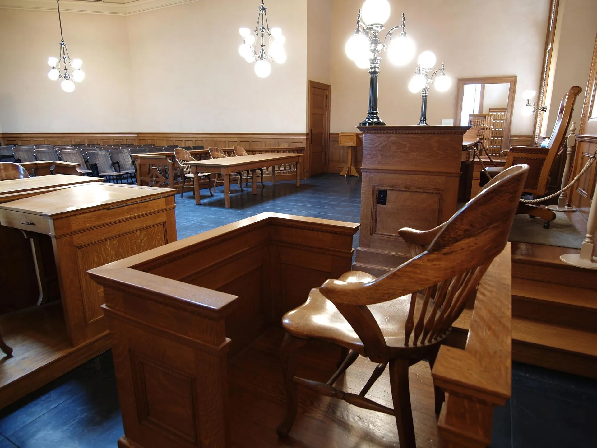 Empty classic courtroom with wooden witness stand, judge's bench, and tables.
