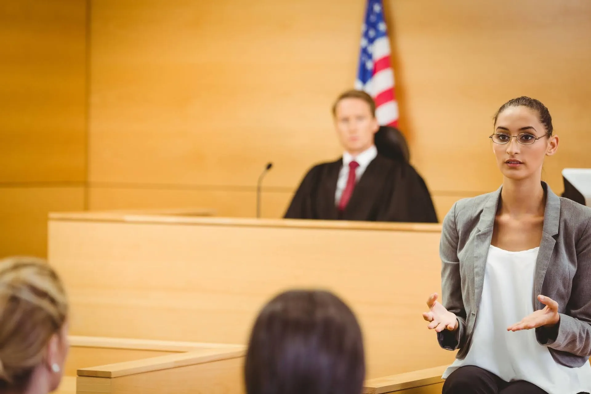 Female lawyer speaking in a courtroom with a judge in the background.
