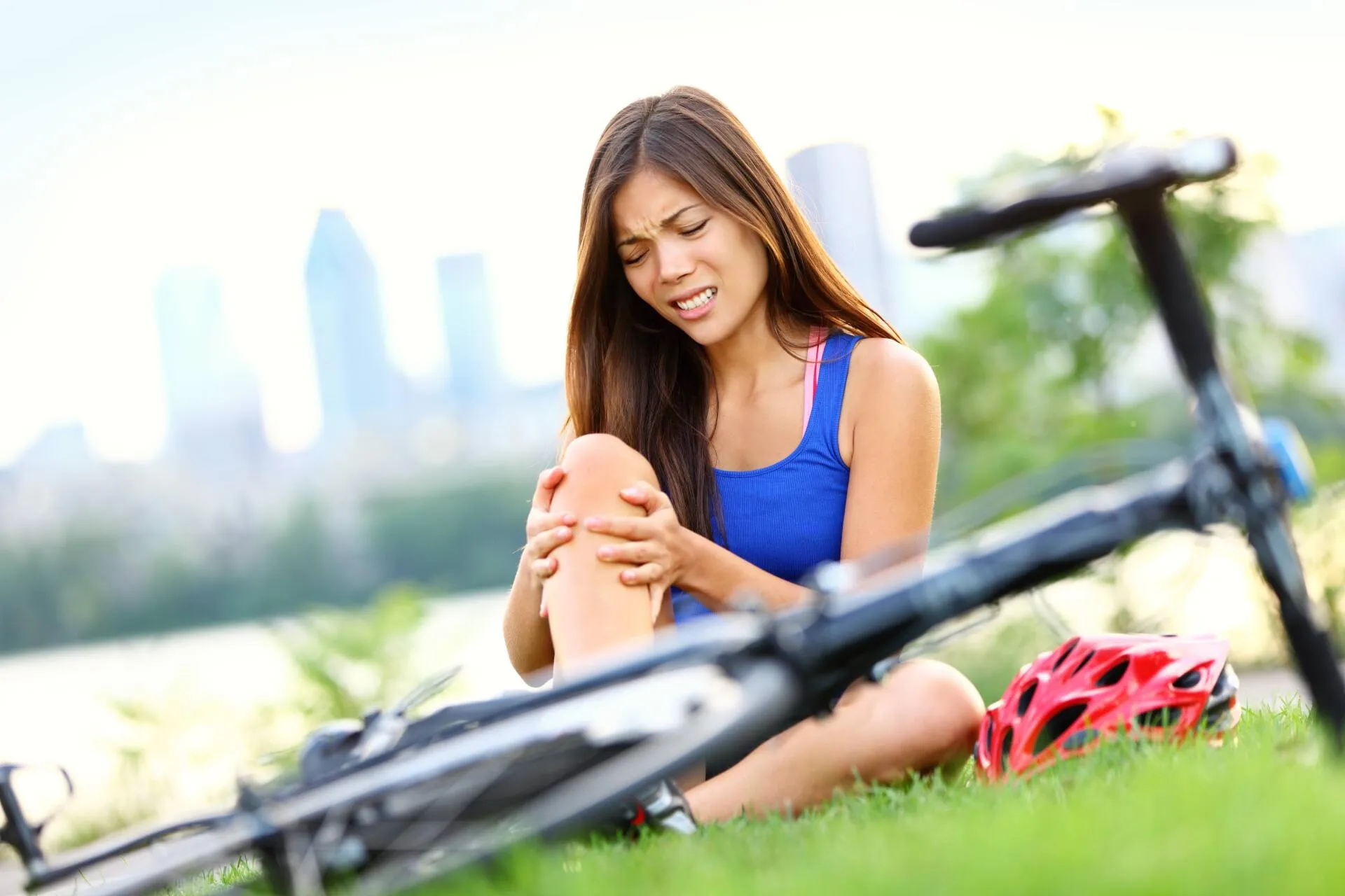A woman holding her injured knee next to a fallen bicycle.