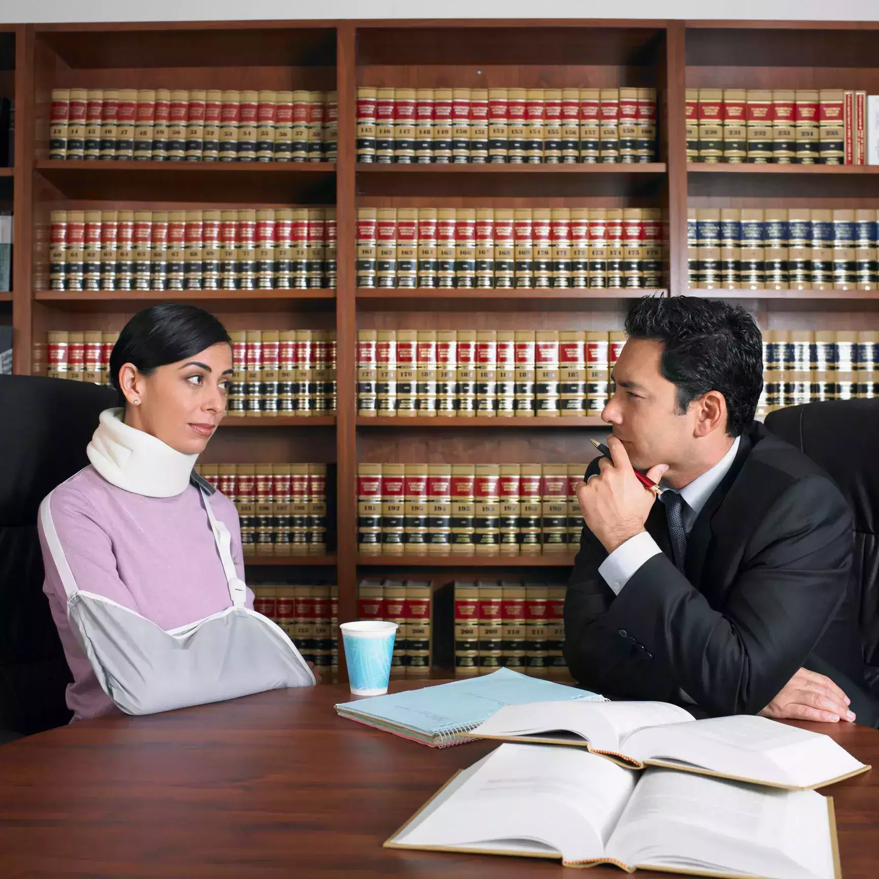 Injured woman with a neck brace and arm sling consulting a lawyer in an office.