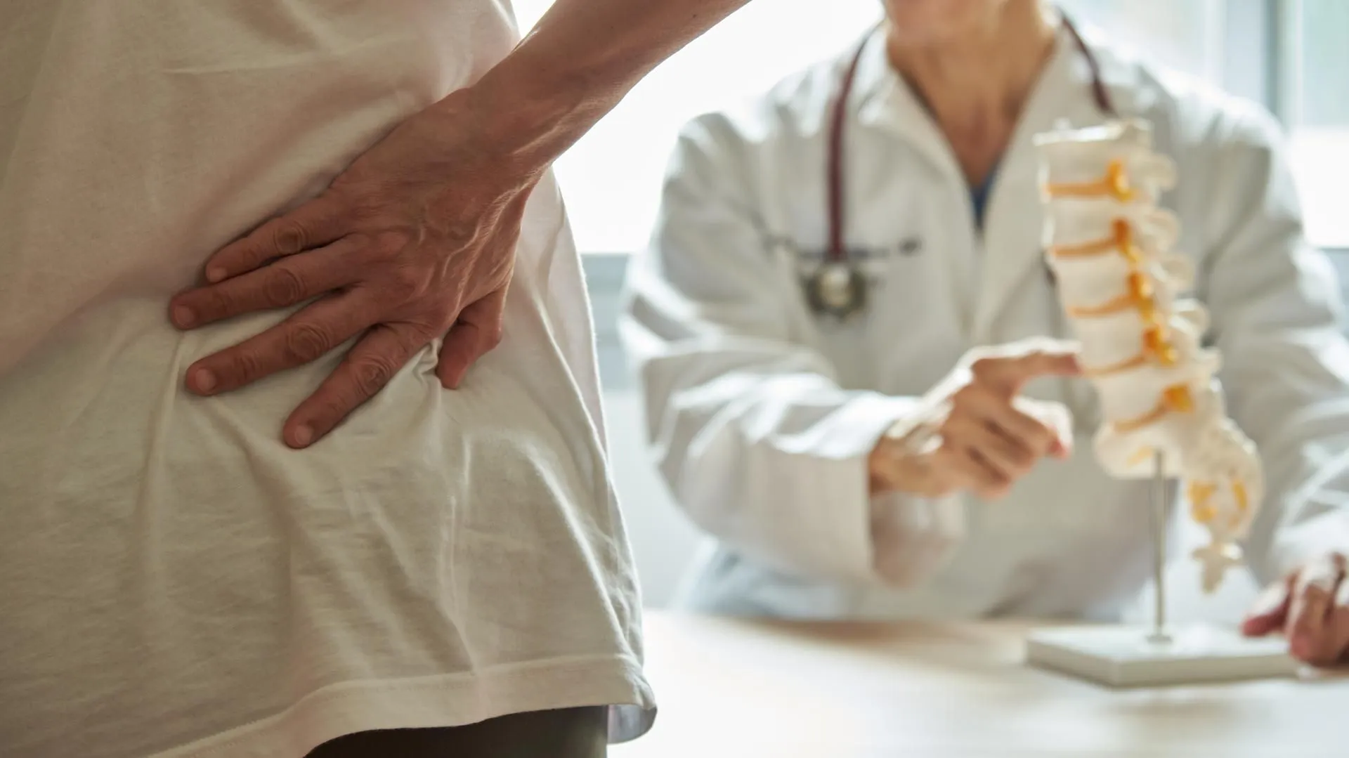 Patient holding lower back while a doctor points at a spine model.