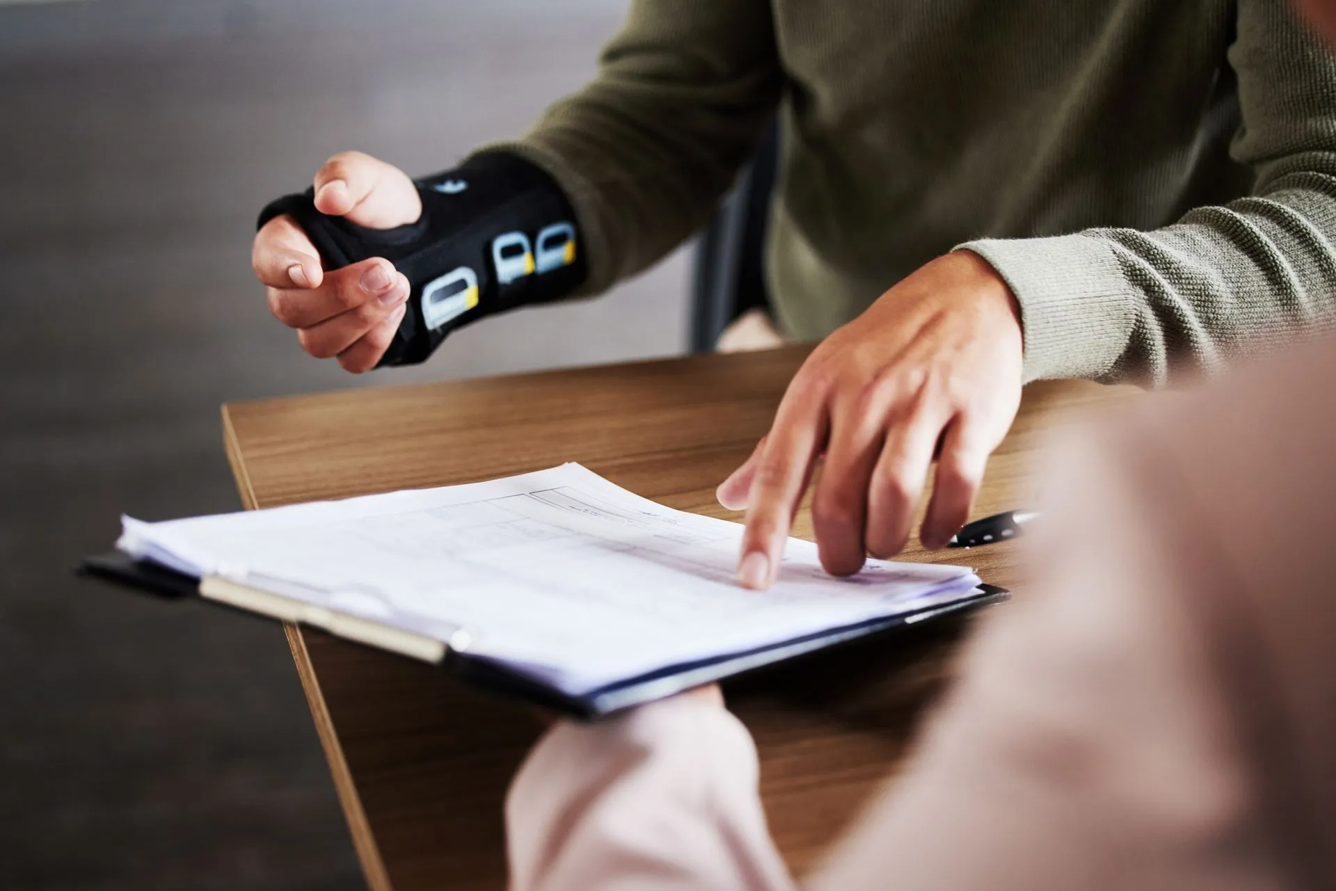 An accident attorney reviewing paperwork with an injured client wearing a wrist brace.