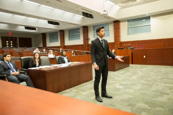 A lawyer speaking in a courtroom with other people.