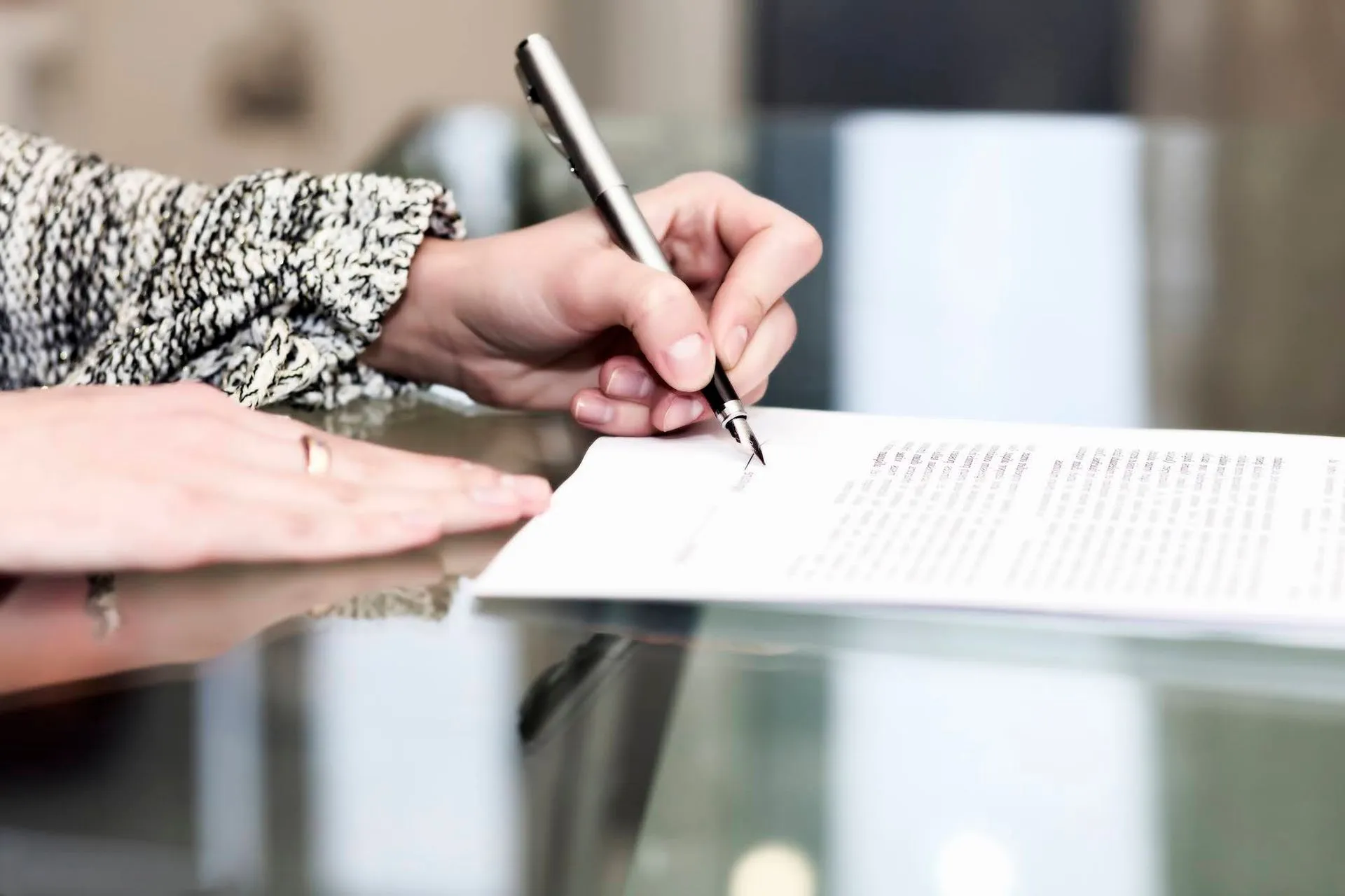 Close-up of hands signing a document with a fountain pen on a glass table.