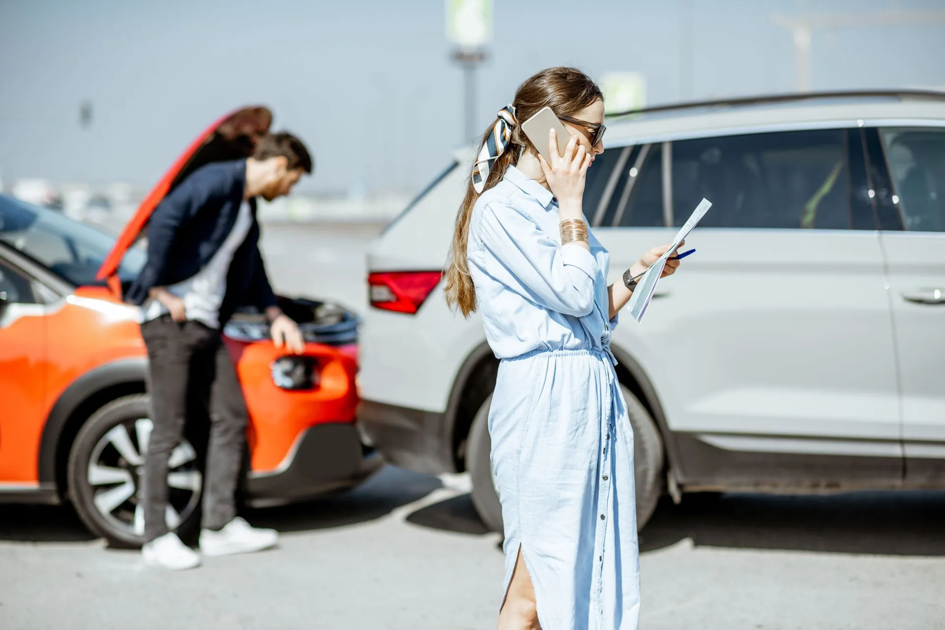 A woman on the phone checking documents after a car crash.