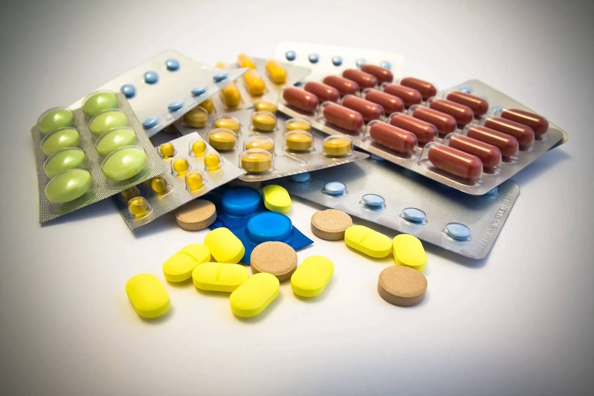 Assorted colorful pills, capsules, and blister packs scattered on a white background.