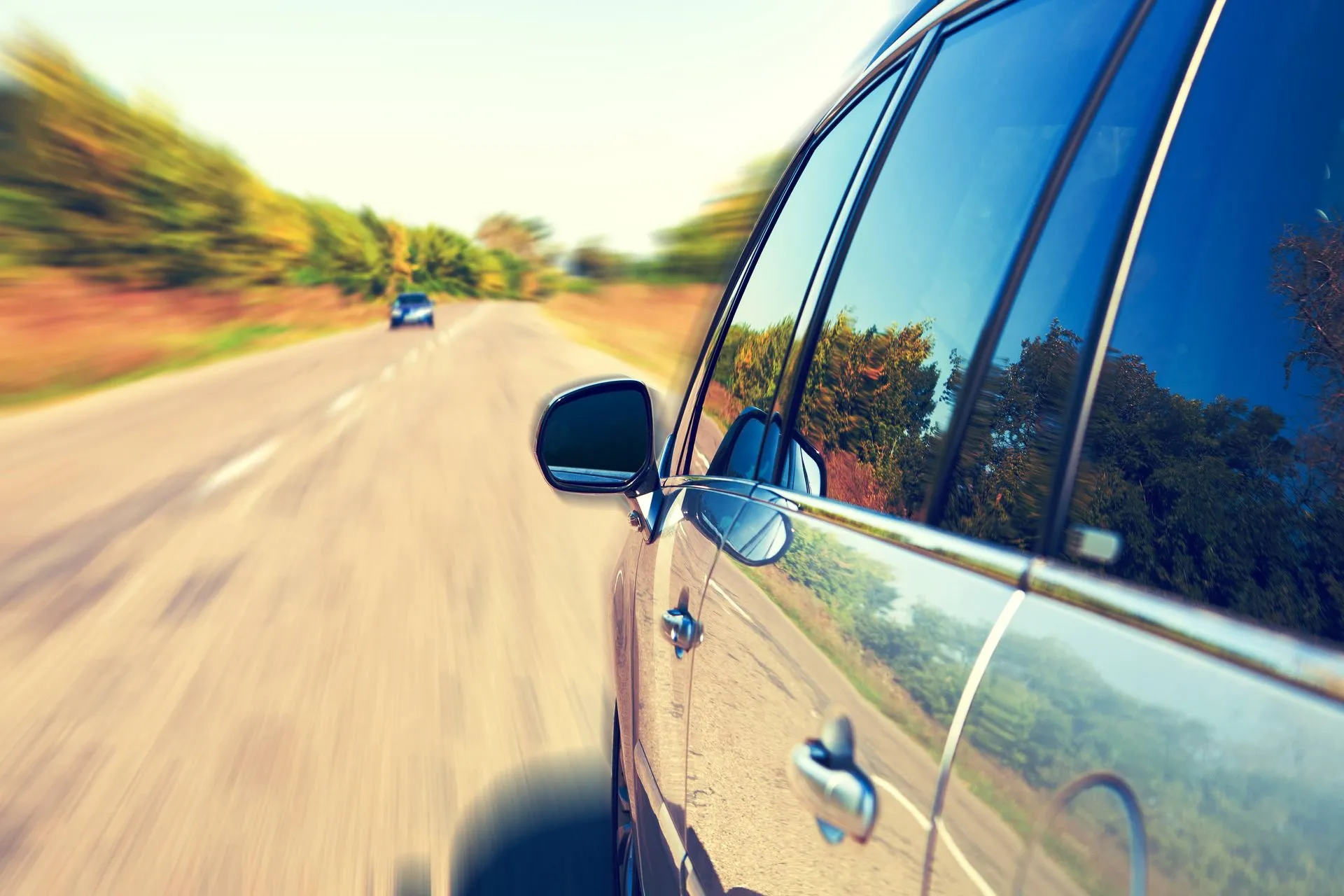 A car driving quickly down a scenic road with trees.