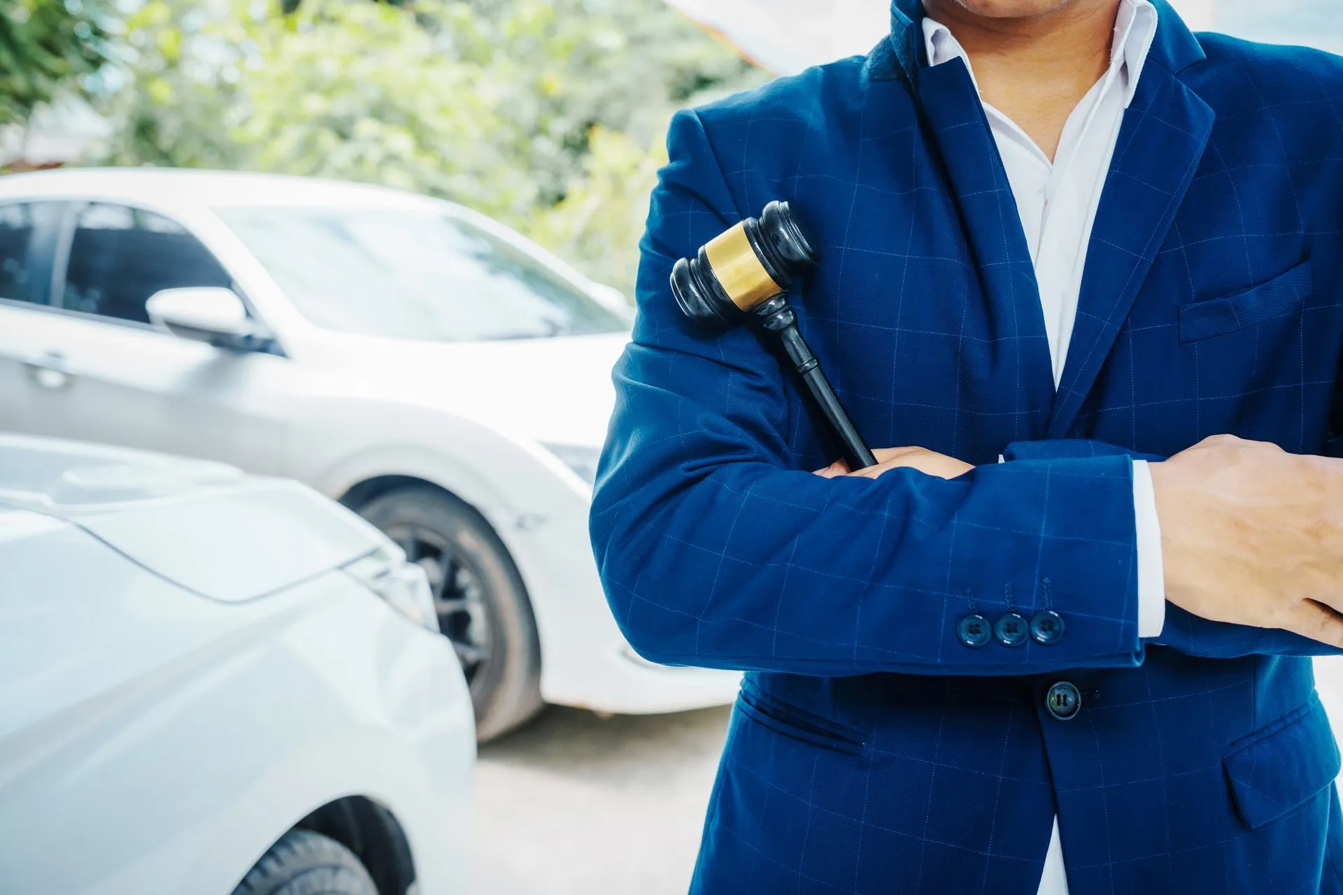 A person in a suit holding a gavel with cars behind.