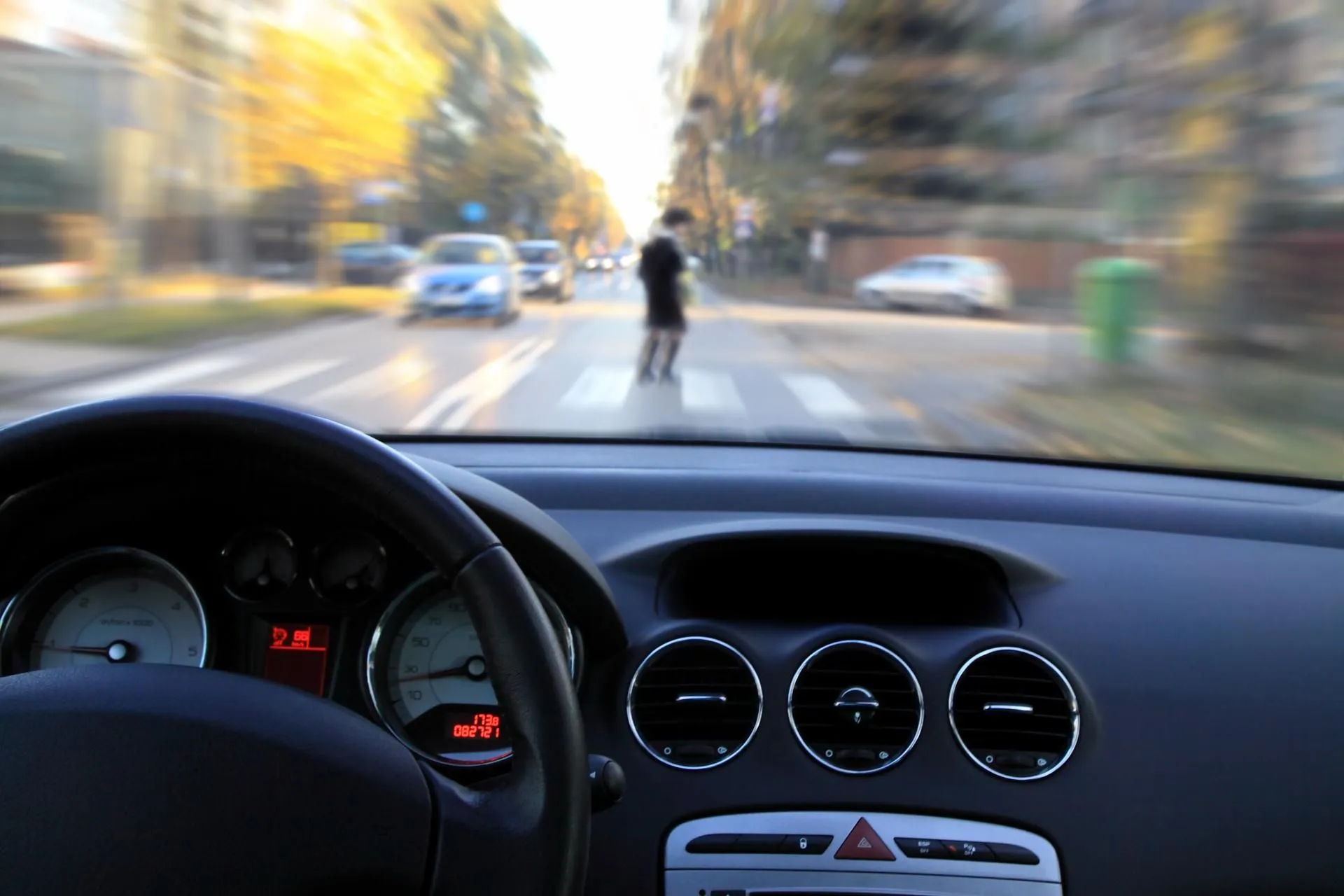 View from a car speeding towards a blurred pedestrian in a crosswalk.