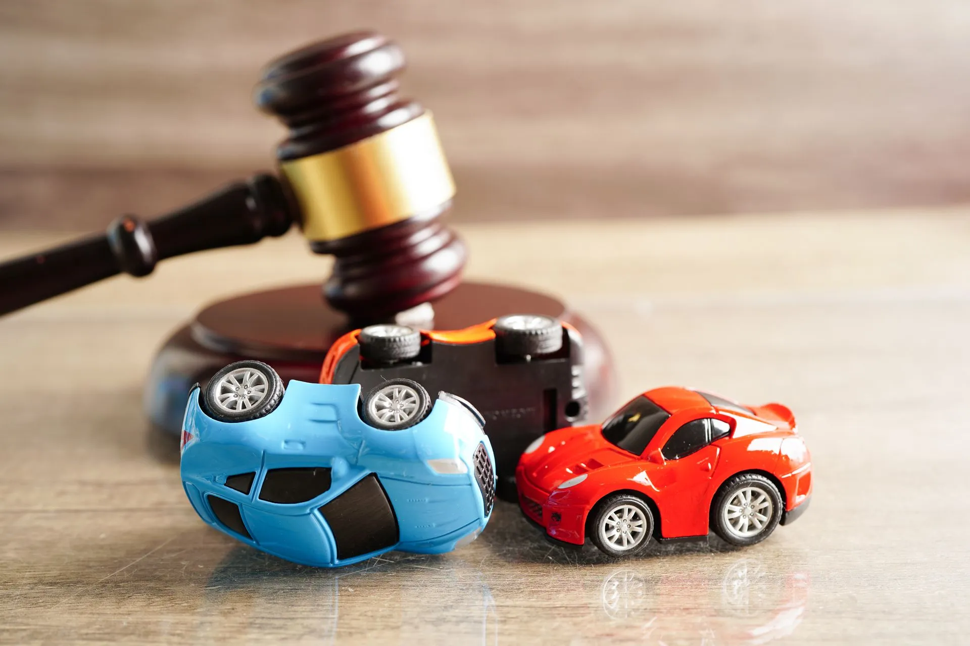 Toy cars in a collision in front of a wooden judge's gavel.