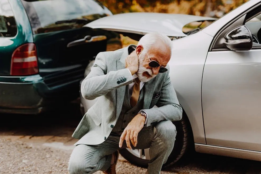 An older man in a suit holding his neck after a crash.