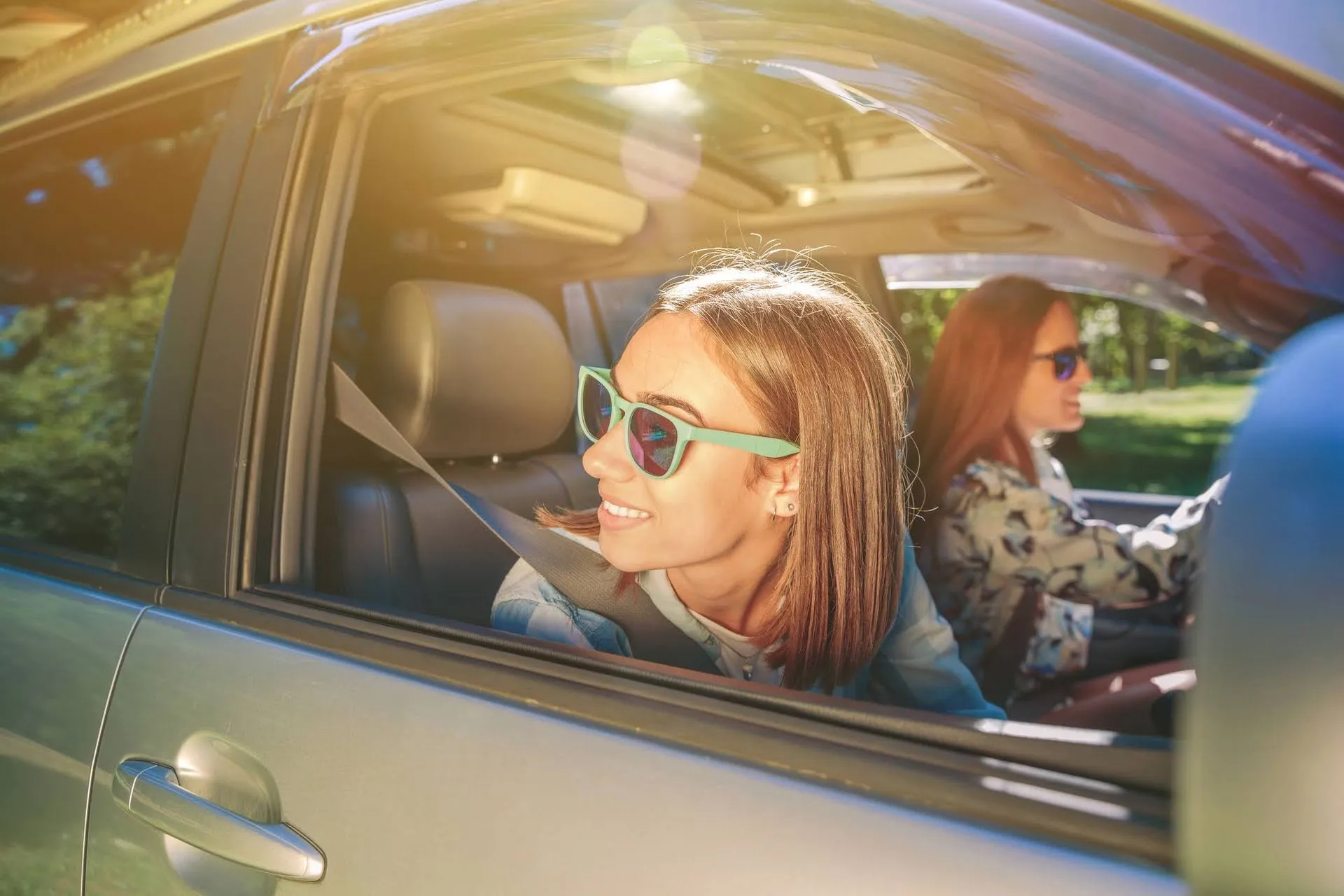 A girl and a woman wearing sunglasses in a car during a trip.