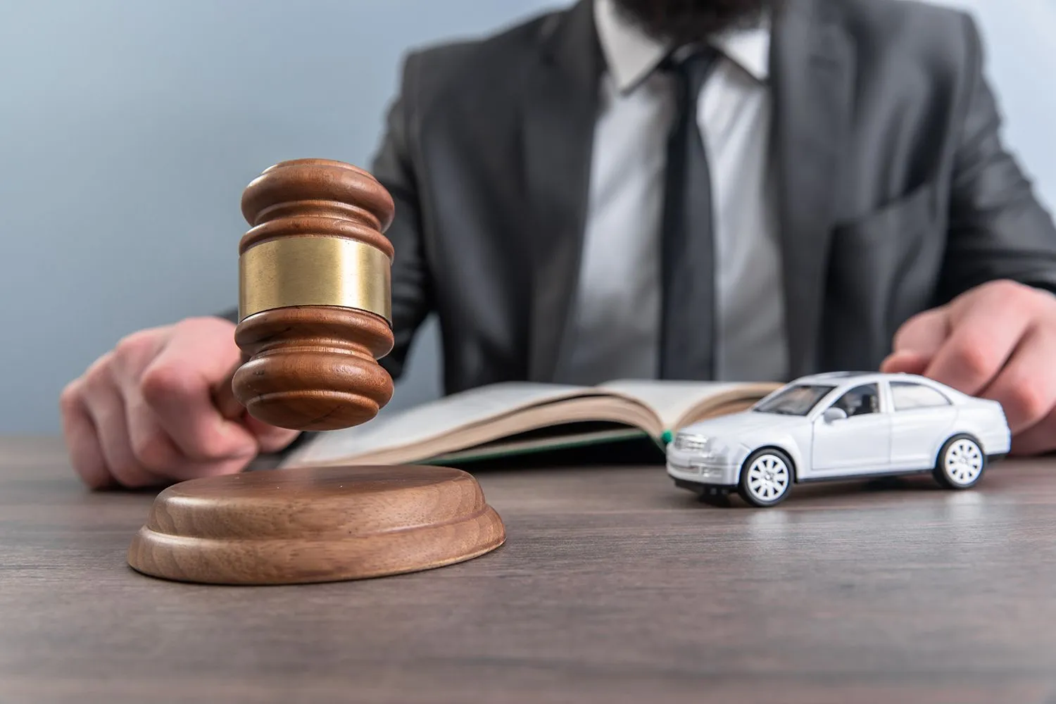 A judge's gavel and a toy car on a desk with a man behind.