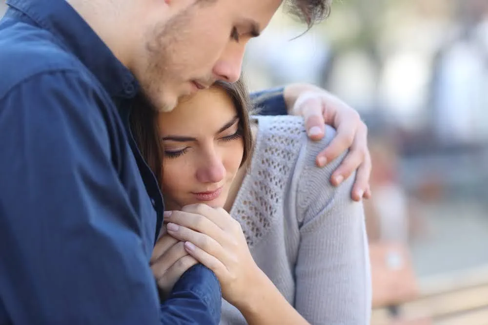 A man comforting and hugging a sad woman outdoors.