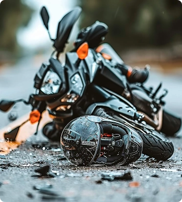 A black motorcycle lies overturned on a paved road with a guardrail and dense green trees in the background.