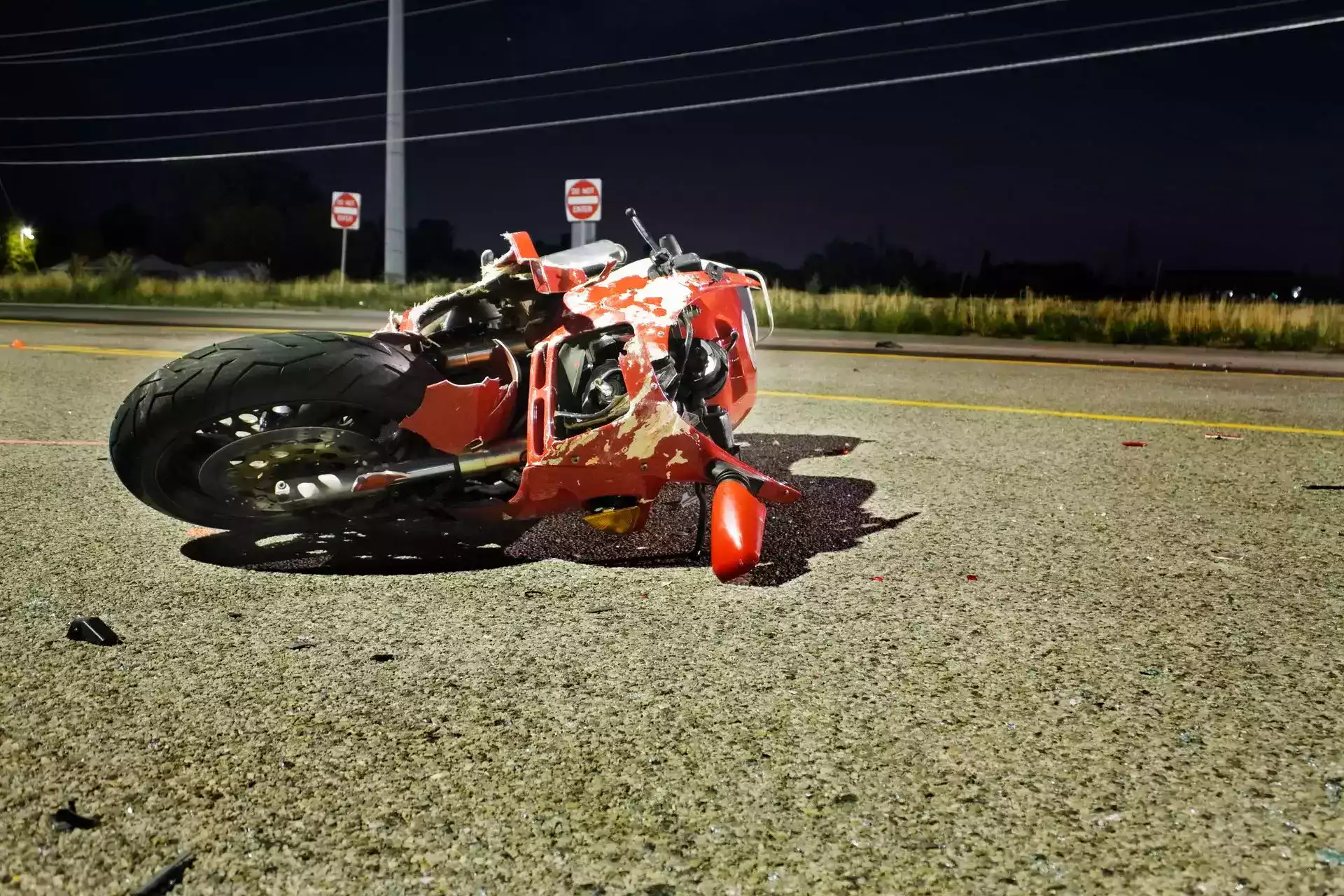 A severely damaged red motorcycle fallen on a night road.