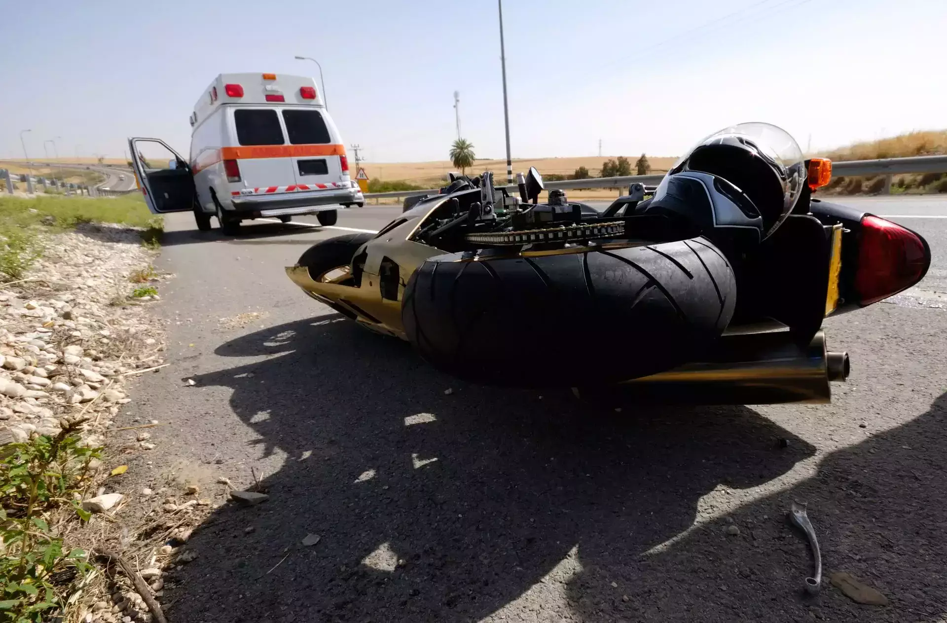 A fallen motorcycle on a road with an ambulance behind.