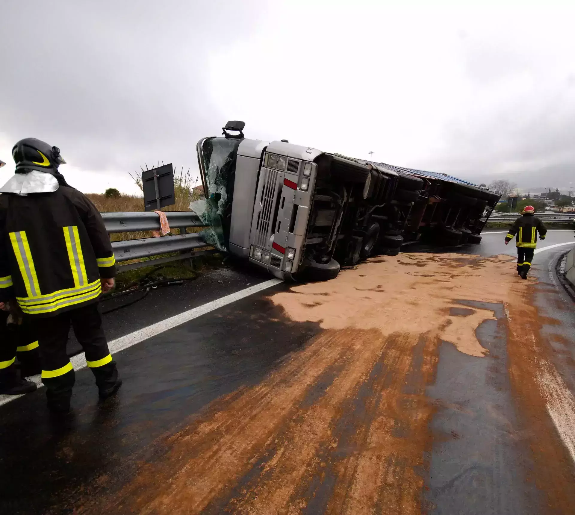 Overturned commercial truck on a wet highway with firefighters responding to the accident.