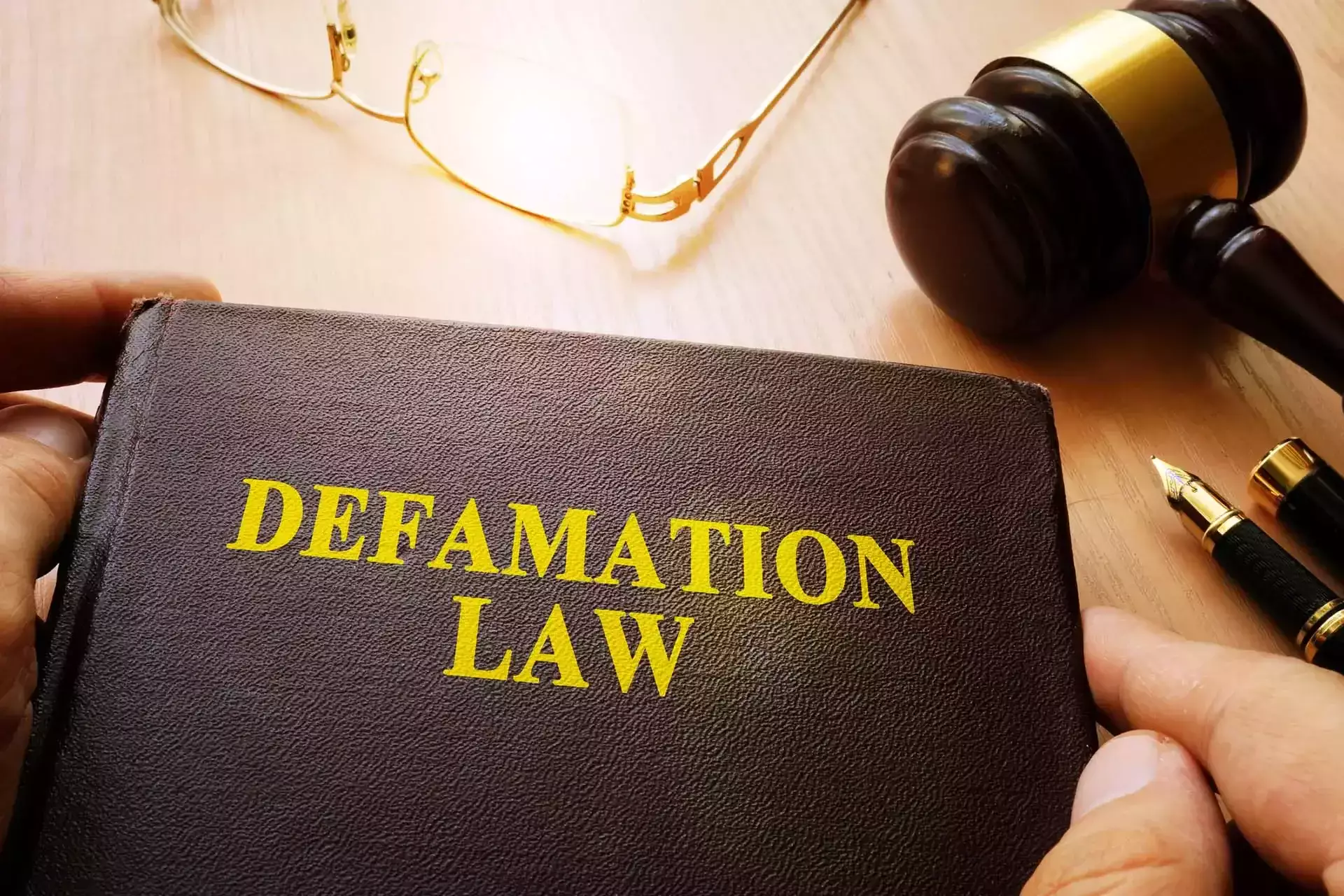 Book with 'Defamation Law' on the cover, near a gavel and glasses.