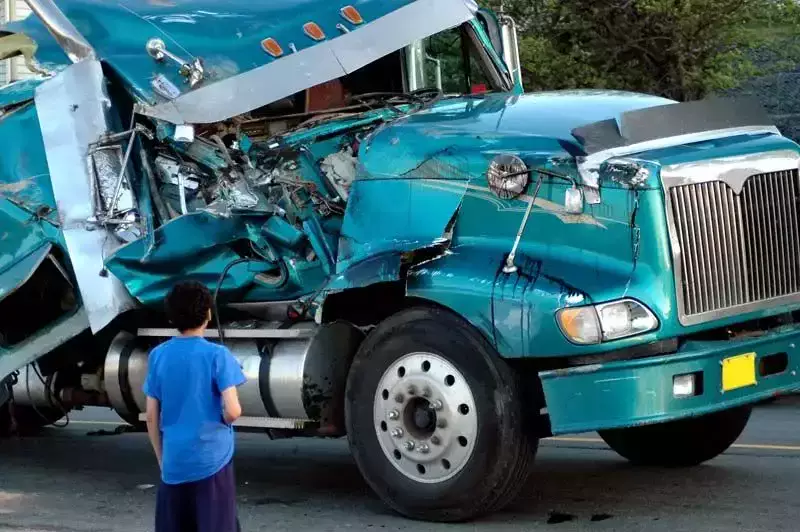 A child looking at a severely damaged green truck on a road.