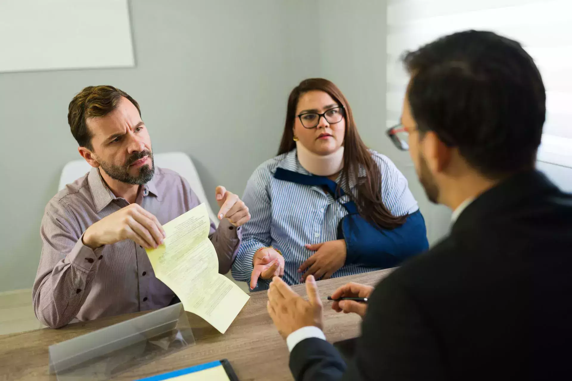Personal injury attorney consulting injured couple reviewing legal documents in office.