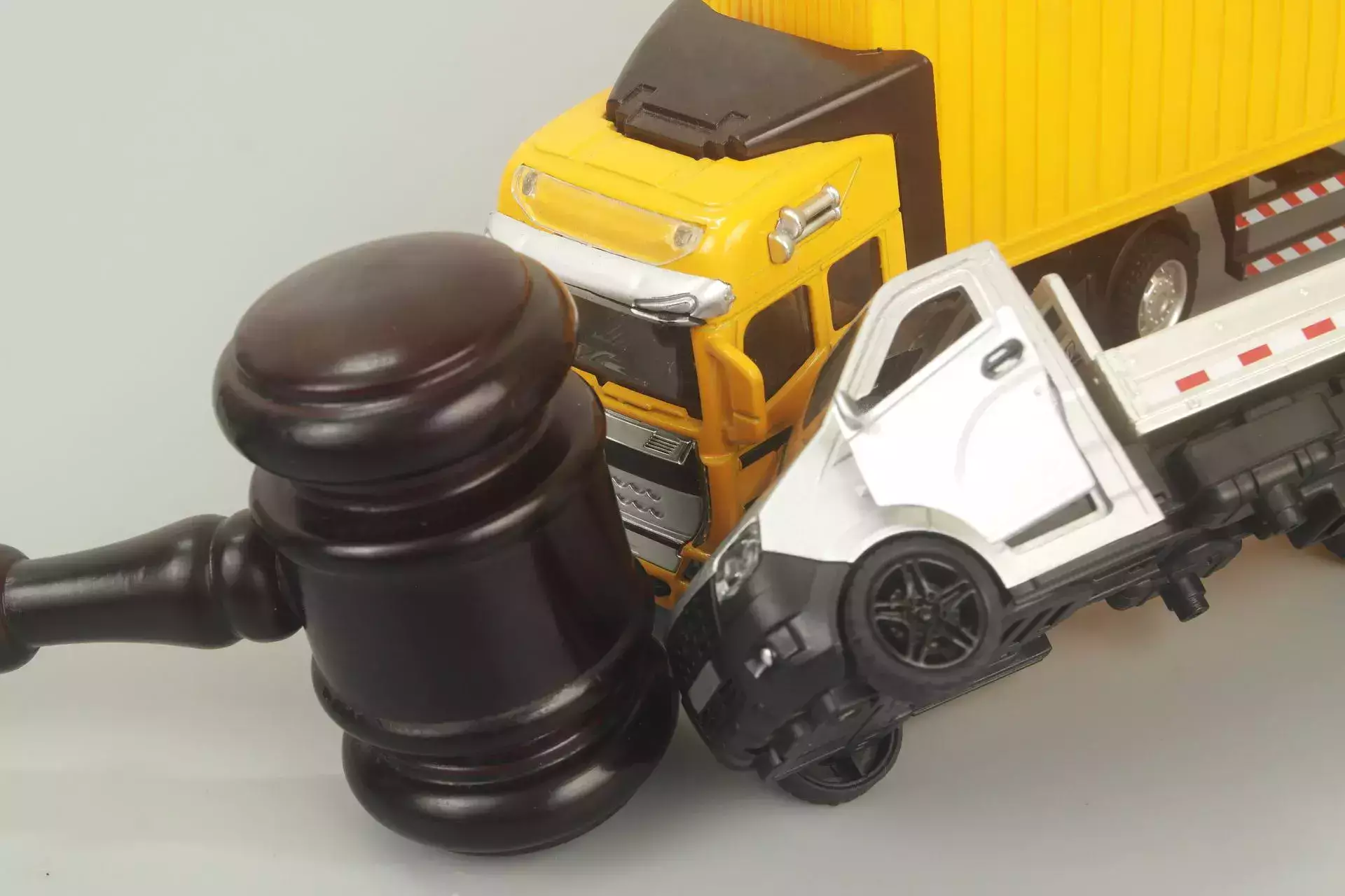 A judge's gavel and toy trucks on a grey background, representing truck accident attorney services.