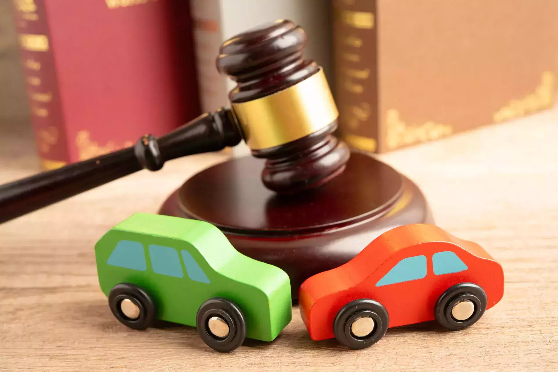 Concepto de abogado especializado en accidentes de tráfico, con coches de juguete de madera junto a un mazo de juez y libros de derecho.