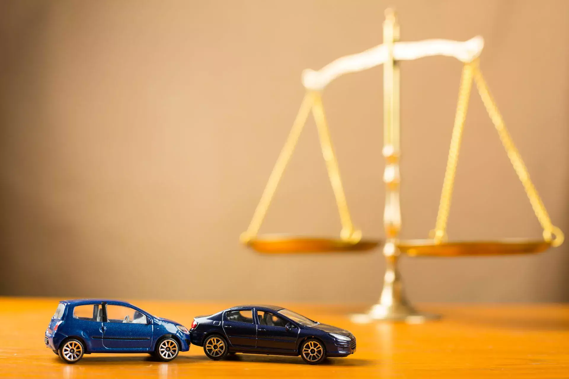 Imagen conceptual de un abogado especializado en accidentes automovilísticos que muestra dos coches de juguete accidentados frente a una balanza de la justicia sobre un escritorio.