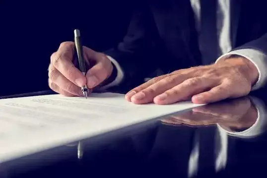 Professional signing a legal document with a pen at a desk