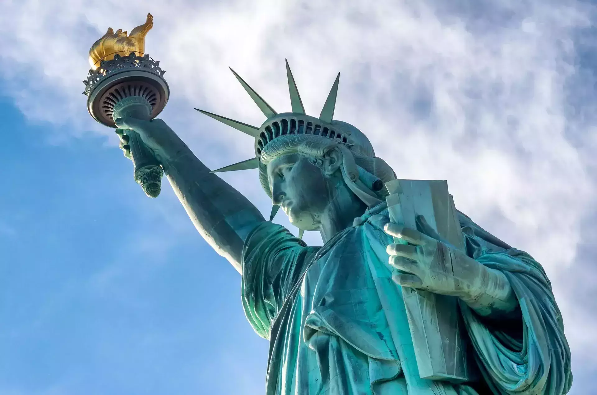 Estatua de la Libertad sosteniendo una antorcha contra un cielo azul y nublado.