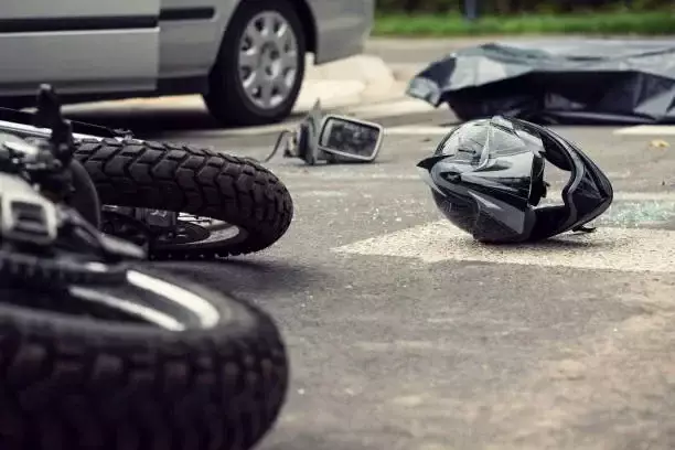 A fallen motorcycle, helmet, and car parts on a road.