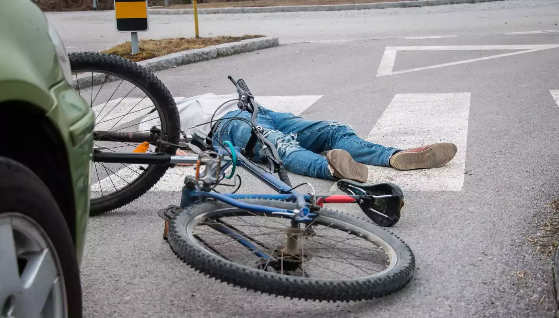 Fallen bicyclist on the road next to a bicycle and a car.