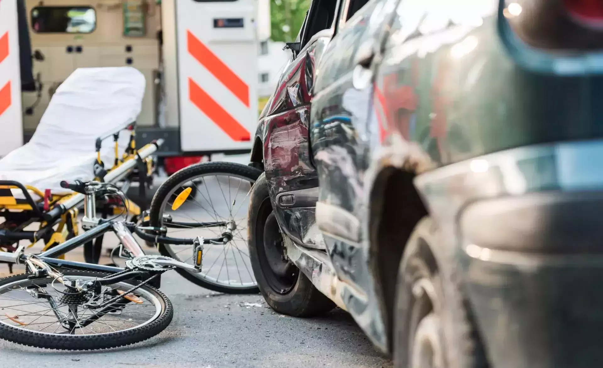 Bicicleta y vehículos dañados en la escena de un accidente de tráfico con una ambulancia cerca.