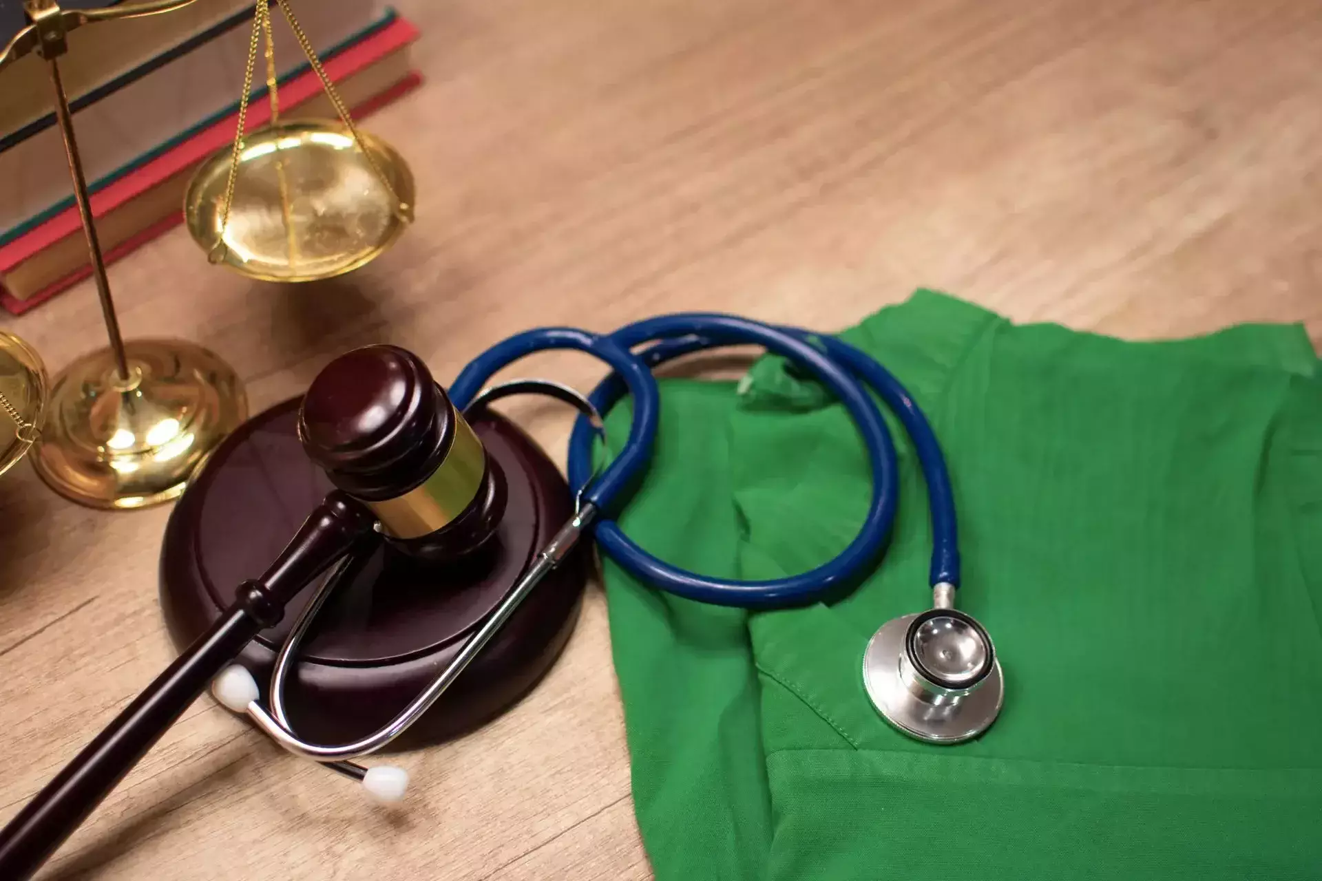 A judge's gavel, stethoscope, and medical scrubs on a wooden desk.