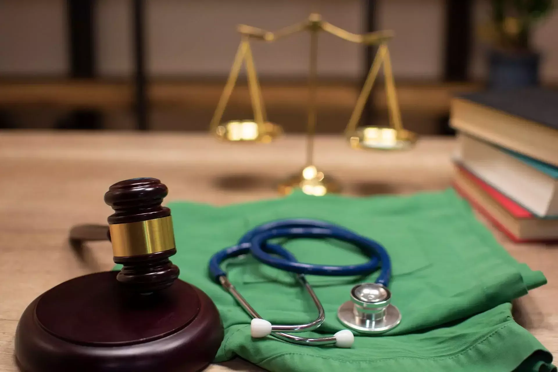 A judge's gavel, stethoscope, and medical scrubs on a wooden desk.