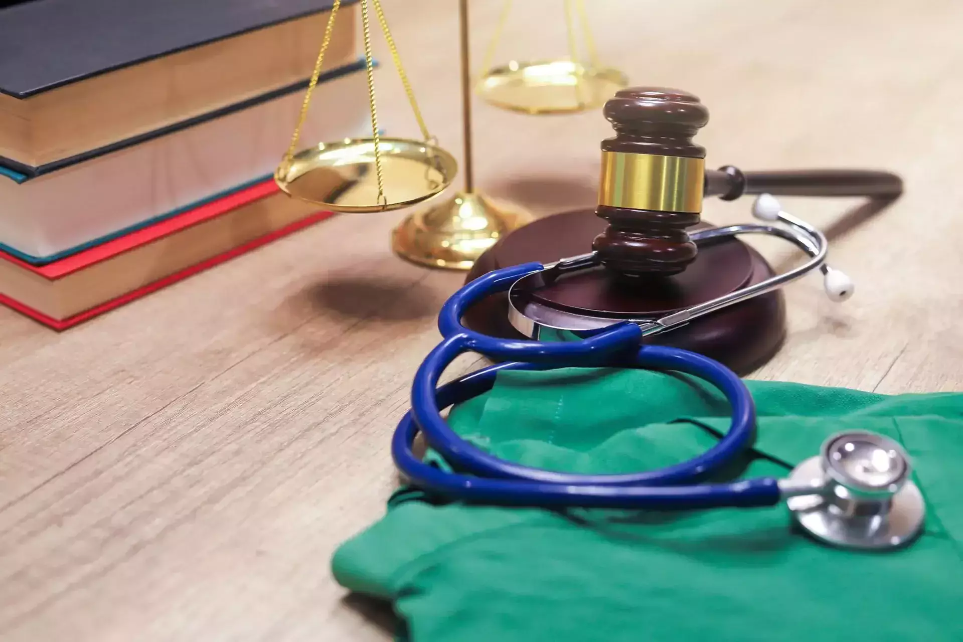 A stethoscope and gavel on a desk with books and scales.
