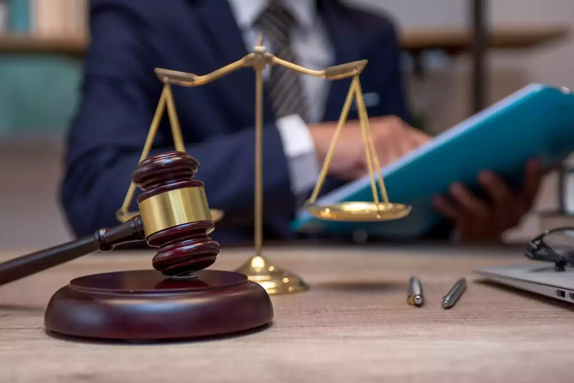 Judge’s gavel and scales of justice with a legal professional reviewing documents in the background.