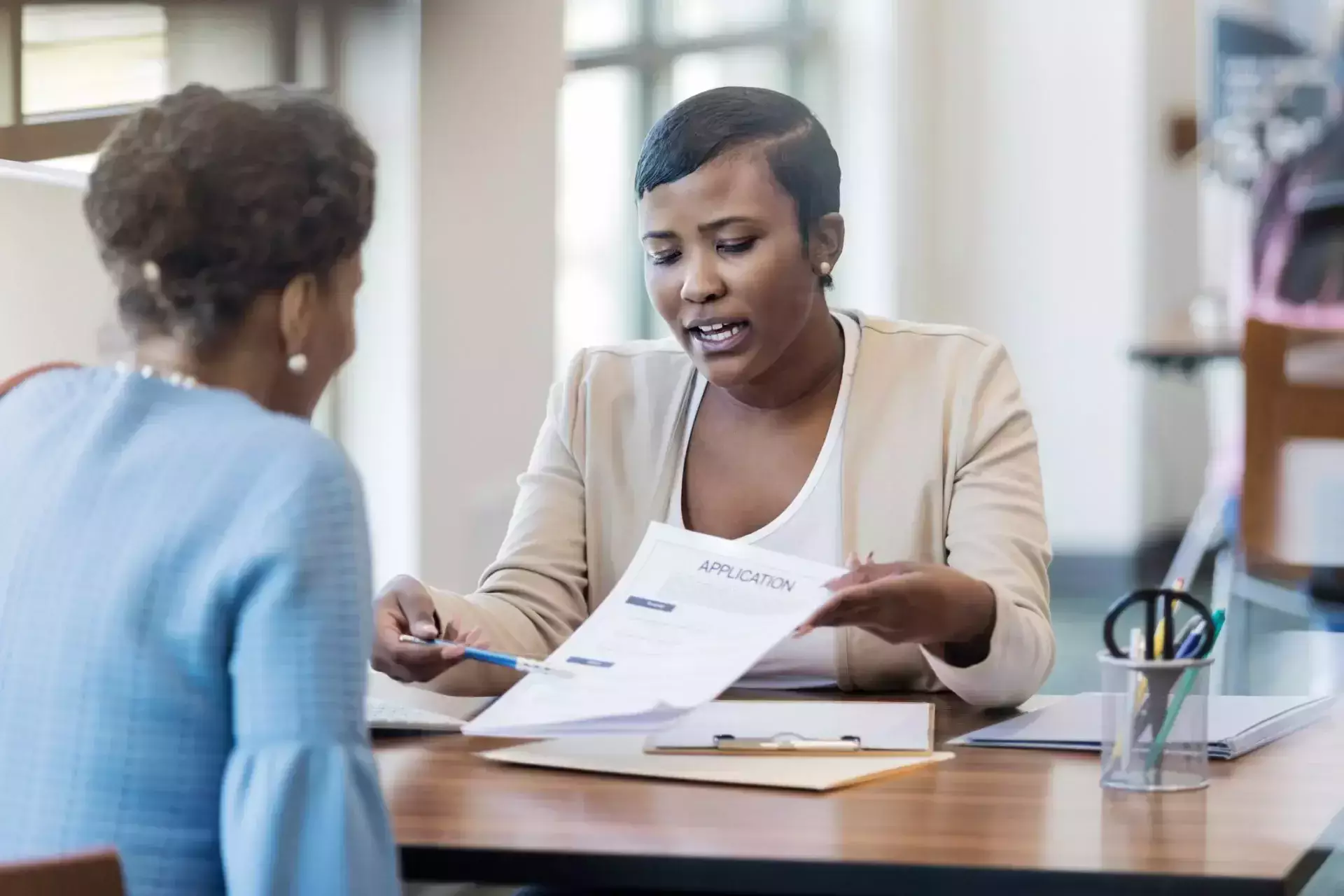 Advisor showing a paper with 'Application' to a woman across a desk.