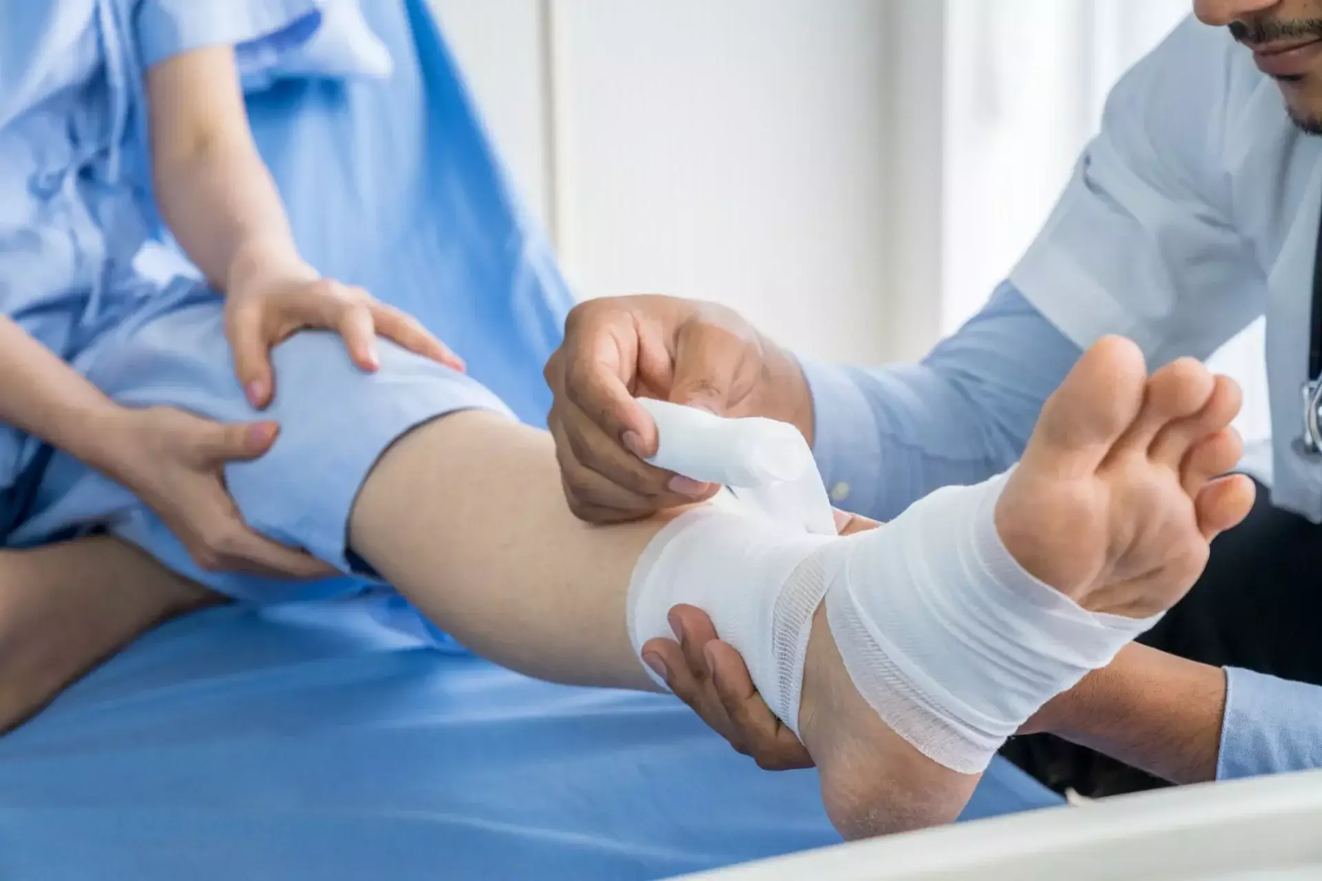 Doctor wrapping a bandage around a patient’s injured ankle in a hospital