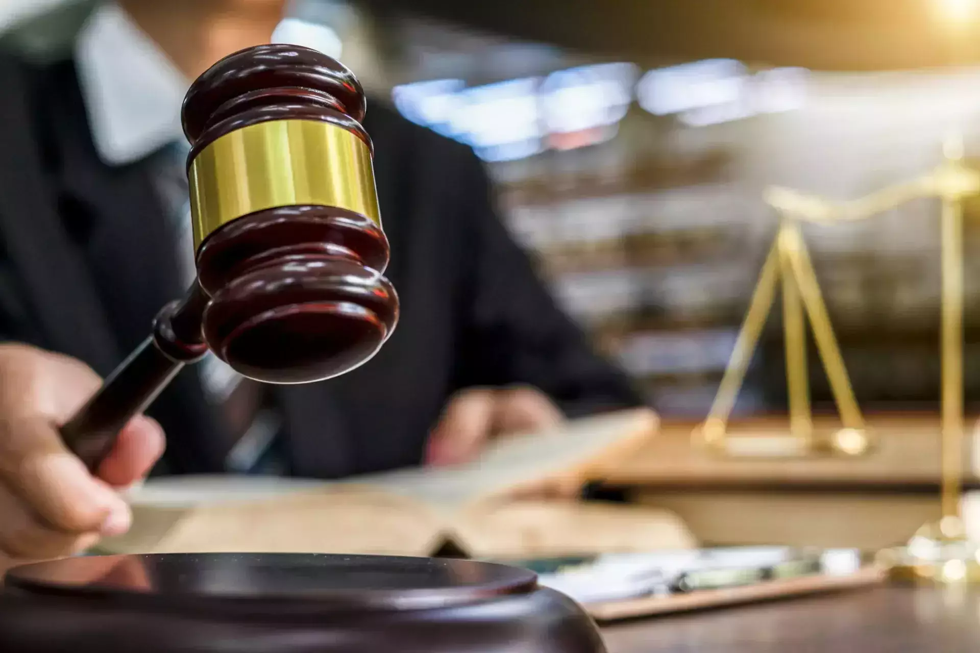 A judge holding a wooden gavel over a block in a courtroom.
