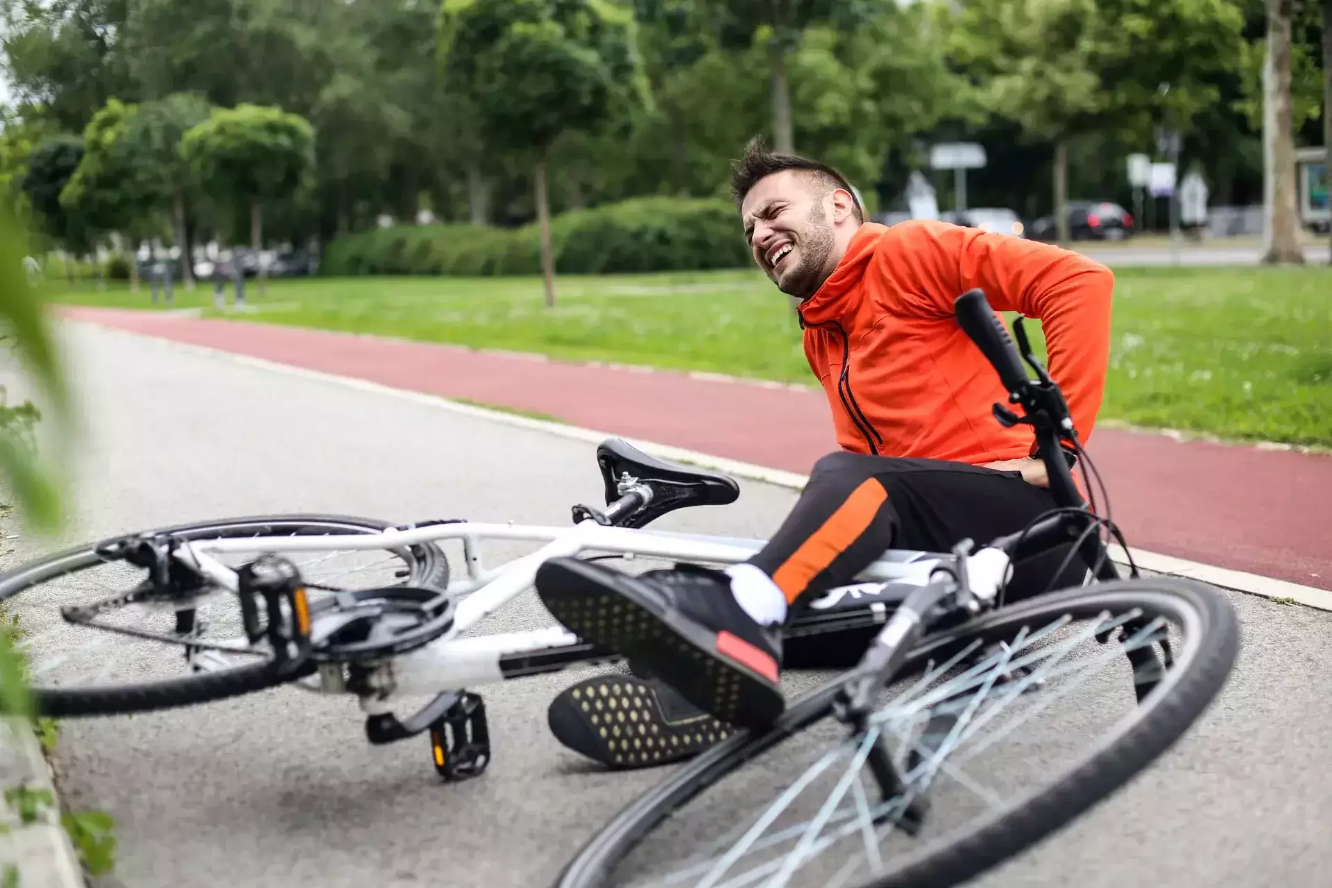 Cyclist in an orange jacket fallen on the road with his bike.