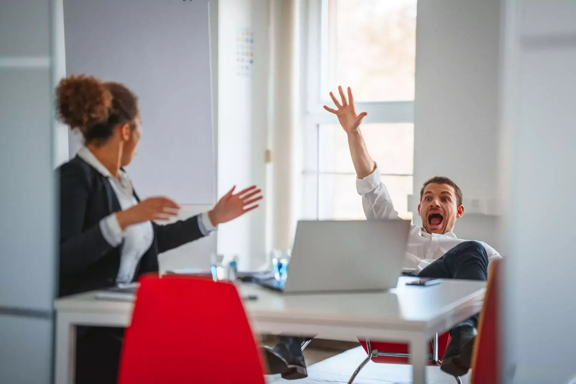 A man falling backward in an office chair while a woman watches.