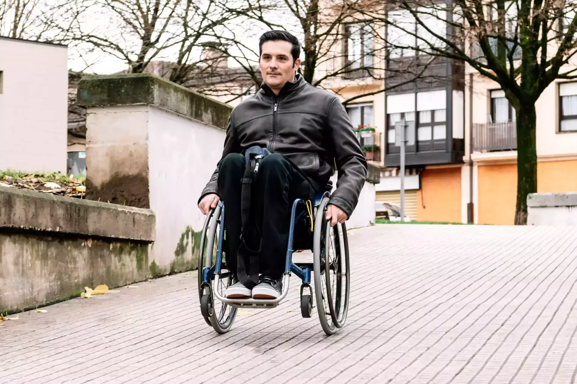 Man using a wheelchair independently on an outdoor paved walkway.