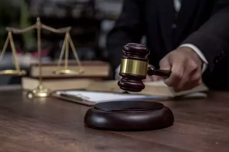 Juez sosteniendo un mazo con una balanza de la justicia y libros de derecho al fondo.