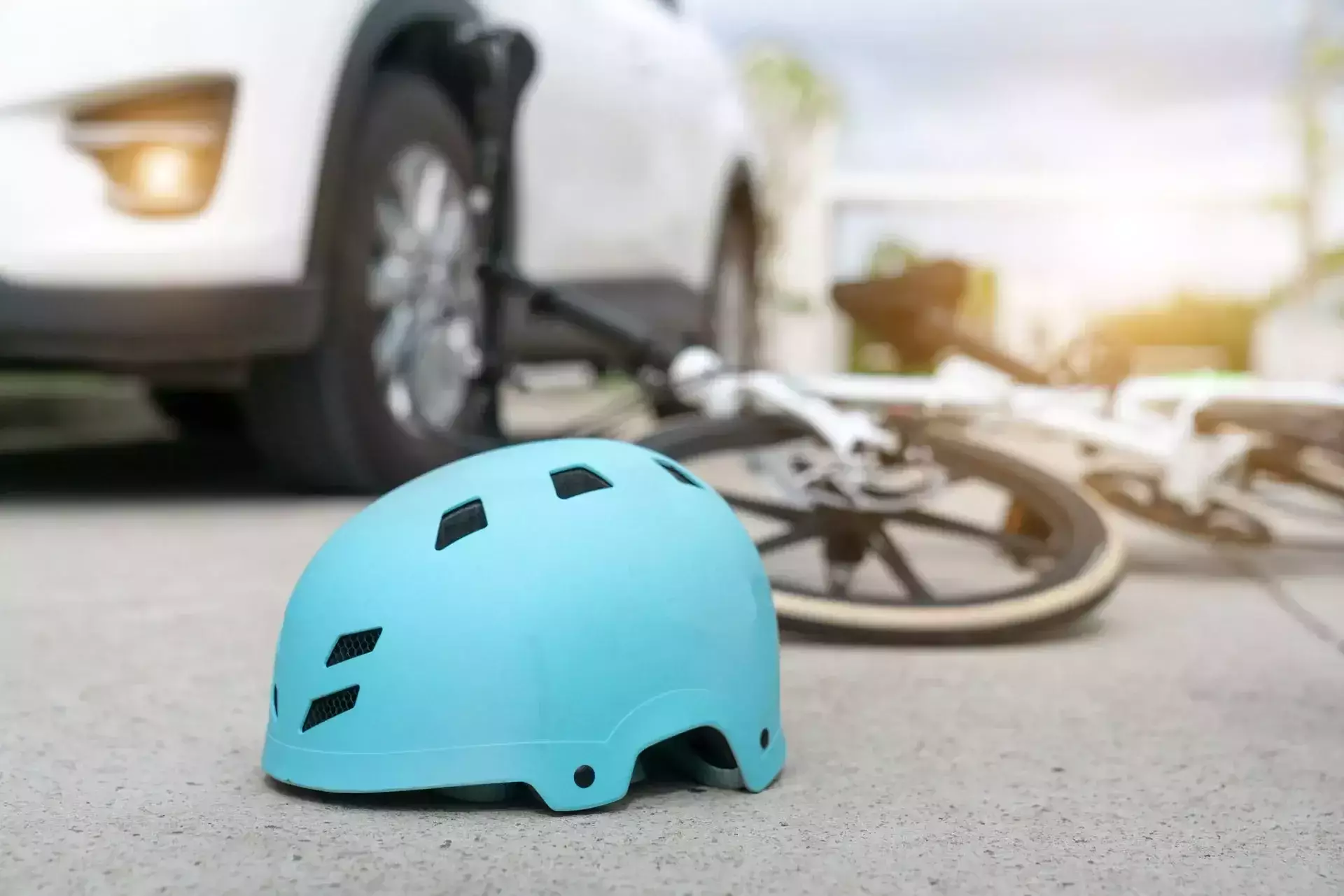 Blue bicycle helmet on pavement with a fallen white bicycle and a white car in the background.